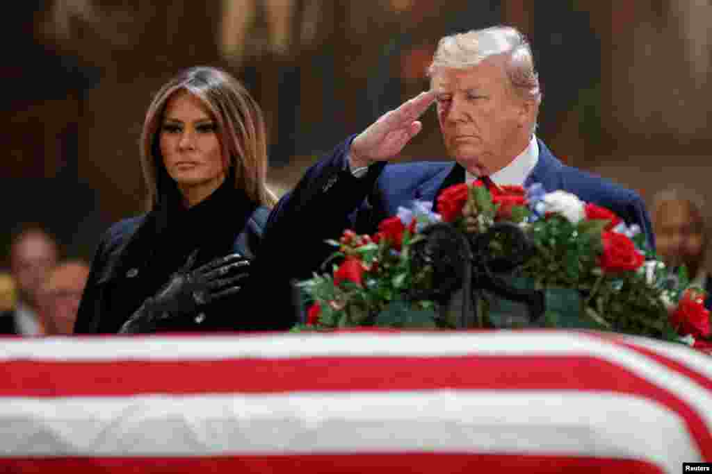 US President Donald J. Trump, with First Lady Melania Trump, salutes the casket containing the body of former US President George H.W. Bush in the Rotunda of the US Capitol in Washington, DC, December 3, 2018.