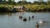 FILE - Refugees, who have fled a flare-up in fighting between the Myanmar army and insurgent groups and settled temporarily on the Moei River Bank, cross the river to receive aid from Thailand on the Thai-Myanmar border, in Mae Sot, Thailand, Jan. 7, 2022