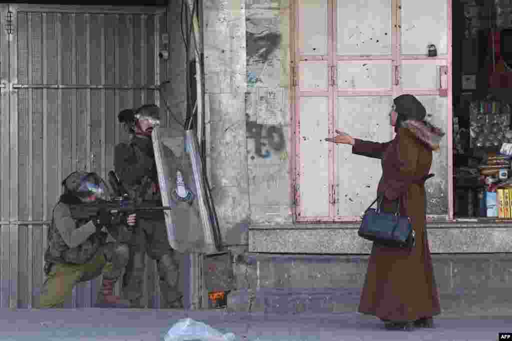 A woman gestures at Israeli security forces firing rubber-bullets to disperse Palestinian stone-throwers amid clashes in the West Bank town of Hebron, Feb. 9, 2022.&nbsp;Israeli forces killed three Palestinians on Feb. 8 during a daytime raid against what Israel described as a &quot;terrorist cell&quot;, leaving a vehicle in the West Bank city of Nablus riddled with bullet holes.&nbsp;