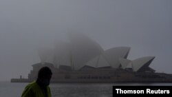 A man wearing a protective face mask walks past the Sydney Opera House, seen shrouded in fog, in Sydney, Australia, July 1, 2021.