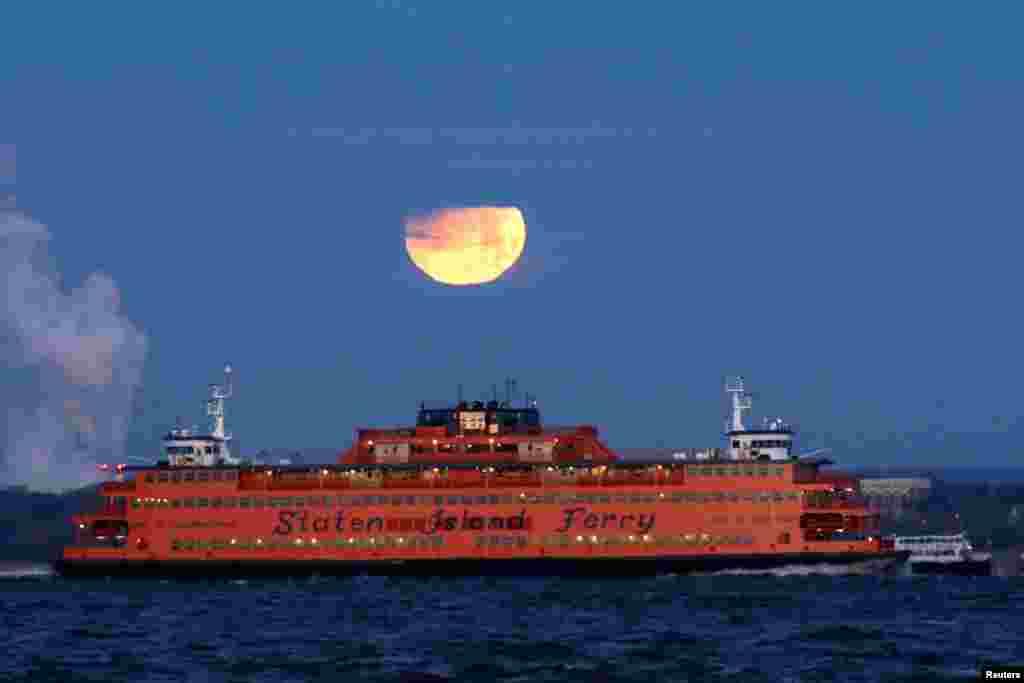 The &quot;Super Blue Blood Moon&quot; sets behind the Staten Island Ferry, seen from Brooklyn, New York.