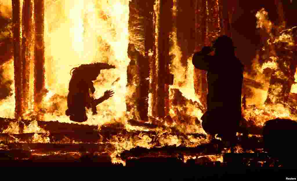 A Burning Man participant (L) falls into the flames of the "Man Burn" after evading the attempted tackles of multiple rangers and law enforcement personnel at the annual Burning Man arts and music festival in the Black Rock Desert of Nevada, Sept. 2, 2017.