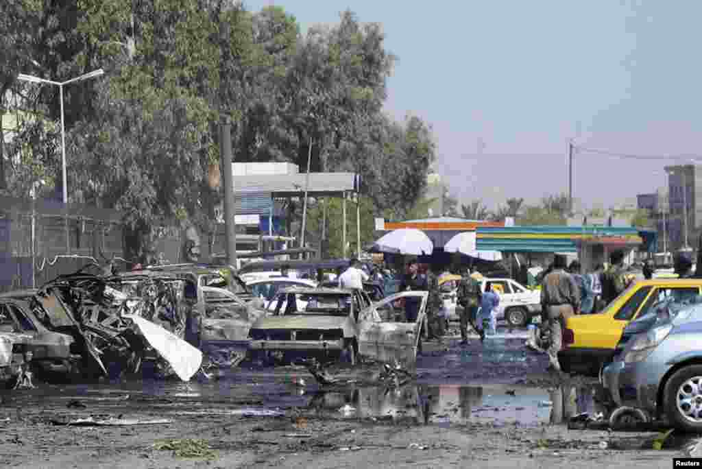 Iraqi security forces inspect damaged vehicles after a bomb attack in Baghdad's Kadhimiyah district, August 15, 2013.