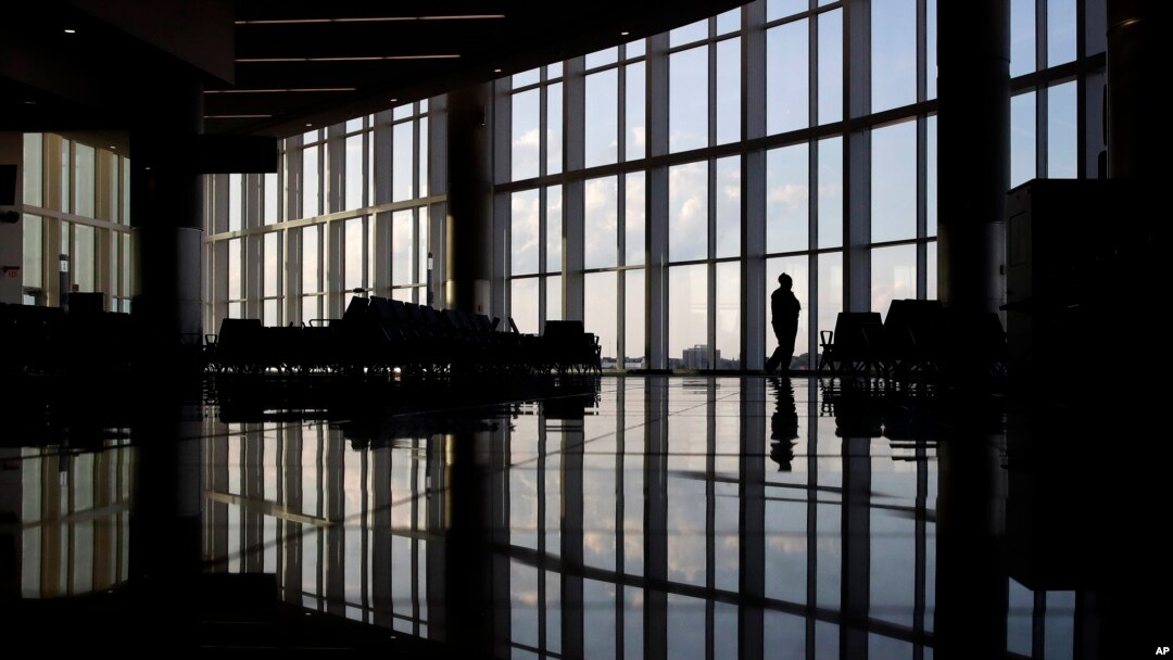 FILE - In this June 1, 2020 file photo, a woman looks through a window at a near-empty terminal at an airport in Atlanta. A new survey found that the coronavirus pandemic has taken a harsh toll on the mental health of young Americans. (AP Photo/Charlie Riedel, File)