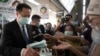 Thailand's Public Health Minister Anutin Charnvirakul, left, distributes masks to commuters during a campaign for wearing masks and washing hands at the skytrain station in Bangkok, Thailand, Friday, Feb. 7, 2020.
