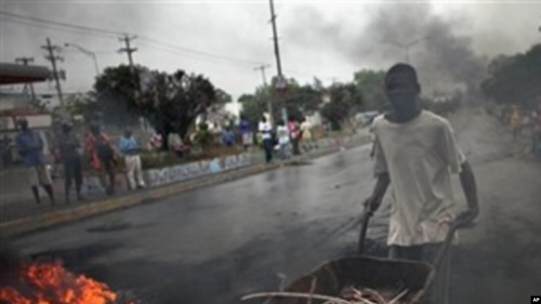 A man pushes a wheelbarrow past a barricade of burning tires in Port-au-Prince, Haiti, Thursday Dec. 9, 2010