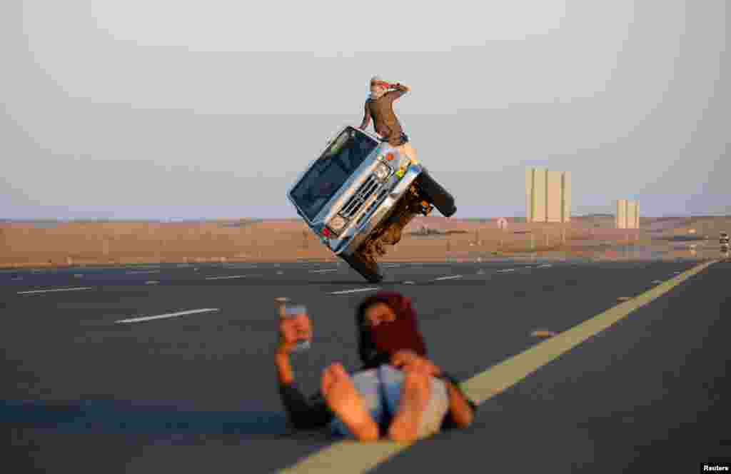 Saudi men perform a stunt known as "sidewall skiing" (driving on two wheels) as a youth takes a selfie in Tabuk, Saudi Arabia, March 11, 2018.