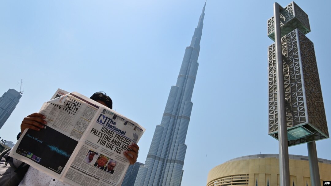 A man reads a copy of UAE-based The National newspaper near the Burj Khalifa in the gulf emirate of Dubai on August 14, 2020, as the publication's headline reflects the previous day's news about Israel. (Giuseppe CACACE / AFP)