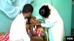A boy suffering from side effects after receiving a measles vaccine, accompanied by his father, is checked by a nurse at Ebolowa regional hospital, in Ebolowa, Cameroon, Dec. 9, 2019. (Moki Edwin Kindzeka/VOA)