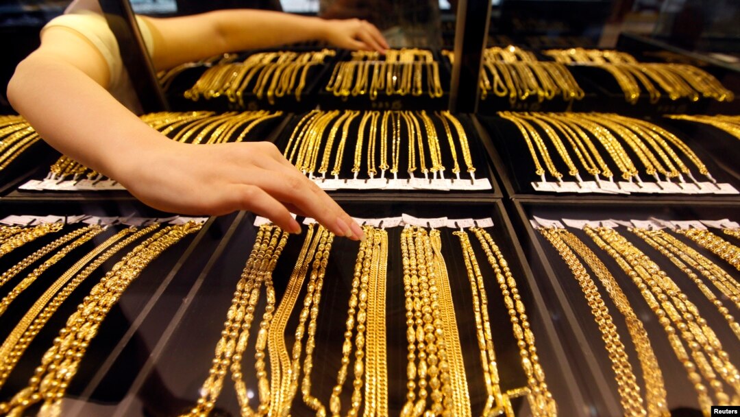 FILE - An employee arranges gold jewelry in a display case as her arm is reflected in the mirror, at a gold shop in Wuhan, Hubei province, Aug. 25, 2011.