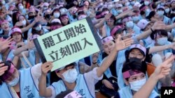 An EVA Air flight attendant holds up a sign which reads: "Strike begins, join immediately" during a protest at the EVA Air headquarters in Taoyuan, Taiwan, Friday, June 21, 2019. 