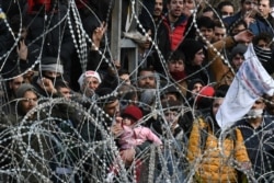 FILE - Migrants who want to cross into Greece from Turkey's Pazarkule border crossing shout slogans as they are gathered at the borderline, in Kastanies, Greece, March 2, 2020.