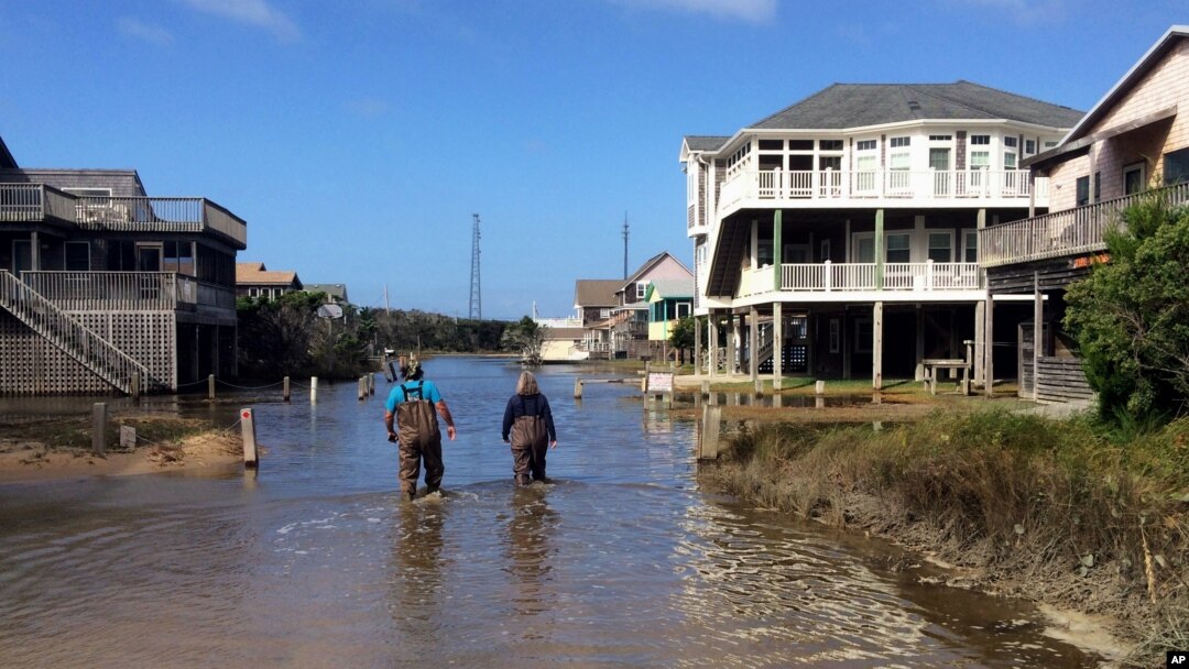 A couple walk along a road flooded with sea water brought by Hurricane Maria in Buxton, N. C., Sept. 27, 2017. Maria has weakened to a tropical storm and is headed east, northeast away from North Carolina.